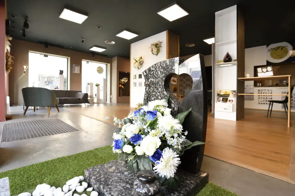Espace d'accueil moderne avec monument funéraire en granit sombre orné de fleurs.