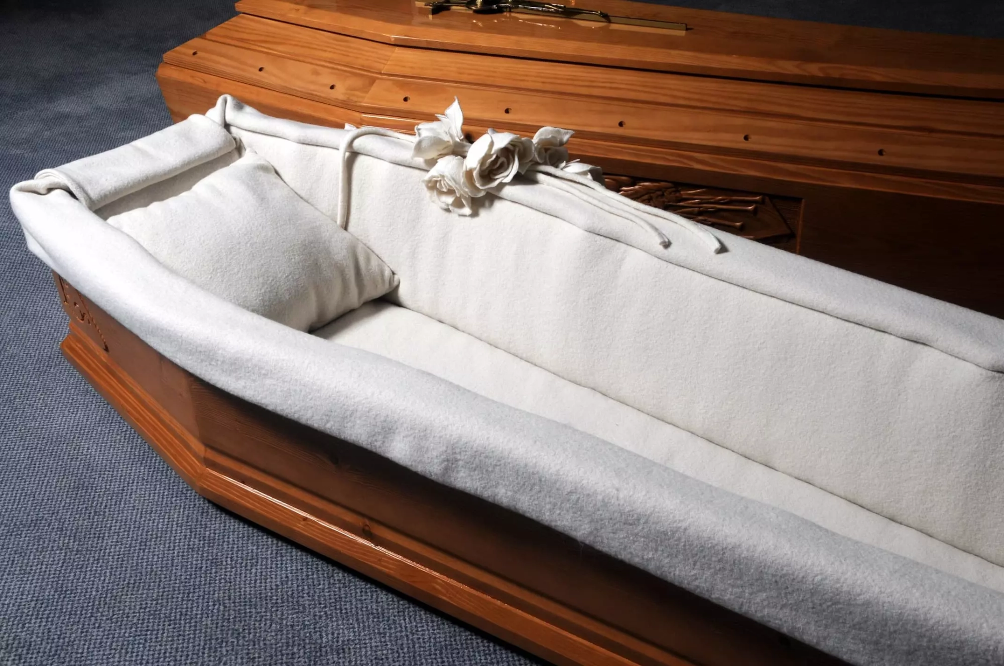 Intérieur d'un cercueil ouvert en bois avec capiton blanc et roses décoratives.